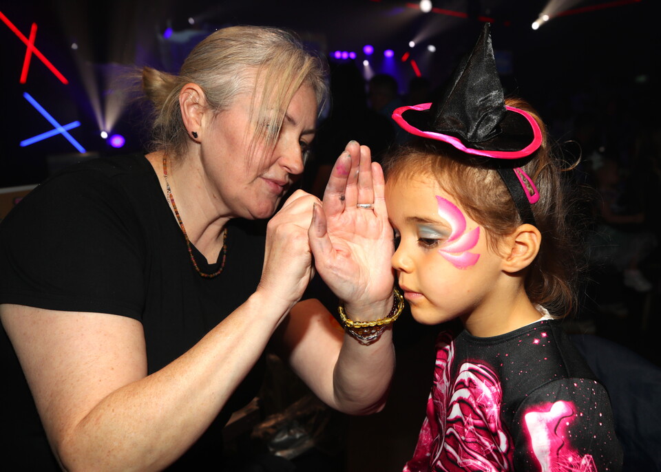 A woman applying face paint to a young girl's face in a dark room.