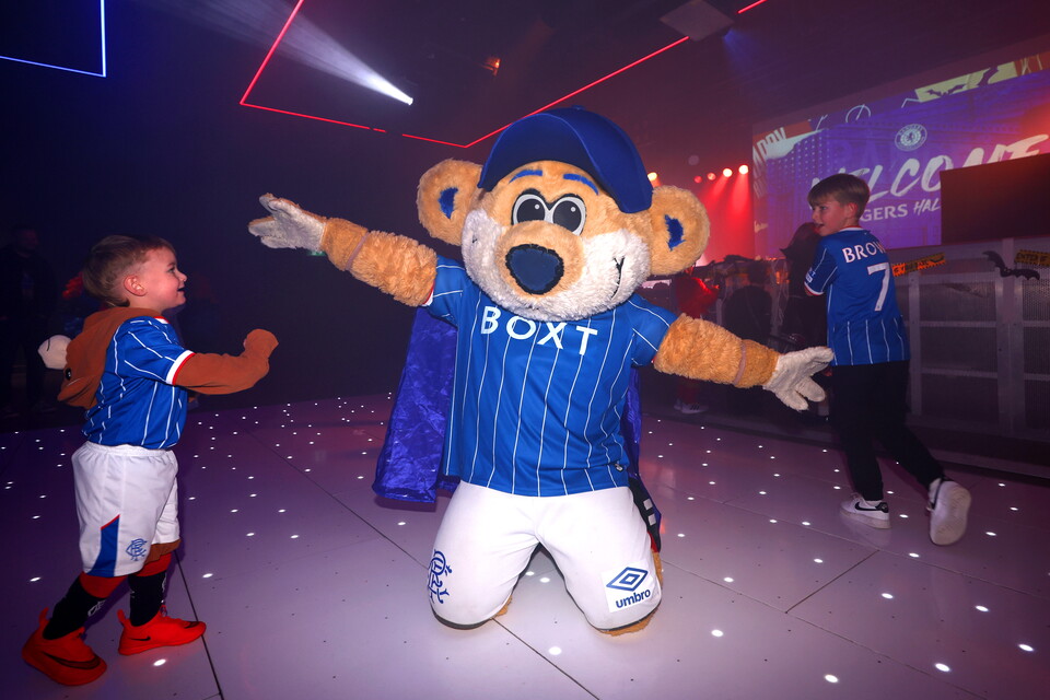 Mascot in blue football shirt with two children dancing in the background