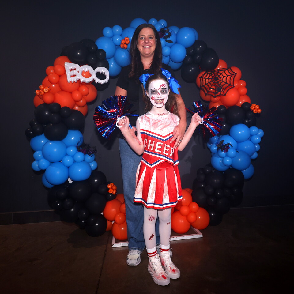 Woman with young cheerleader in costume in front of balloon arch