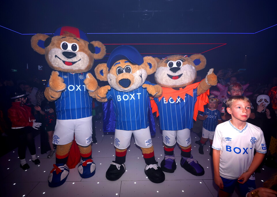 Three mascots wearing blue football shirts and white shorts stand with a child in a white shirt.