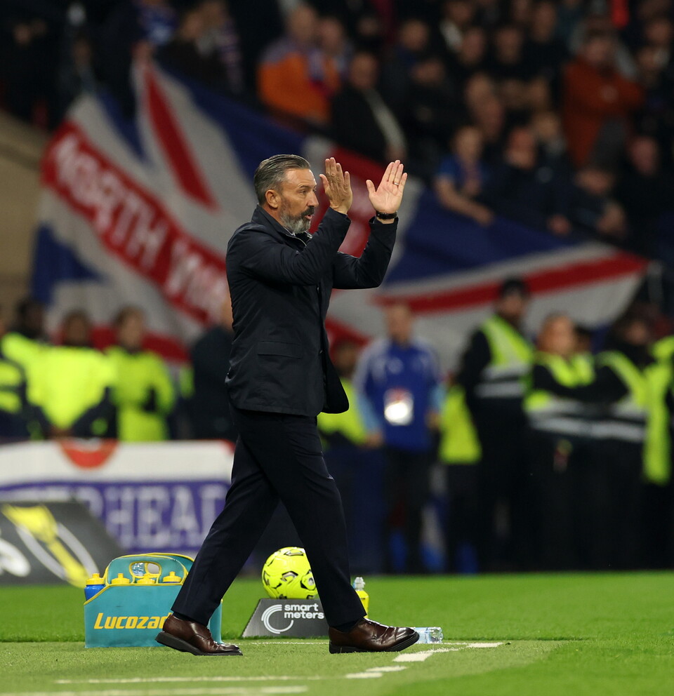A man walks on a football pitch with hands raised as crowd and banners look on