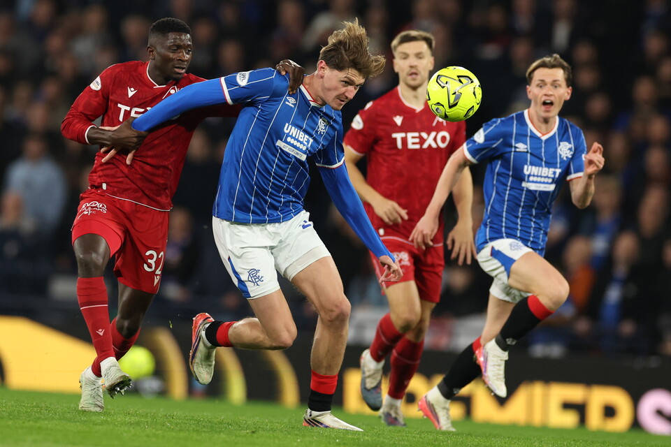 Four football players in action on a pitch with a yellow ball in mid-air.