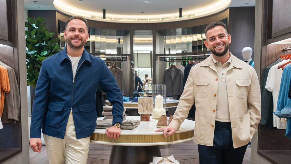 Two men smiling and standing behind a display table in a clothing store