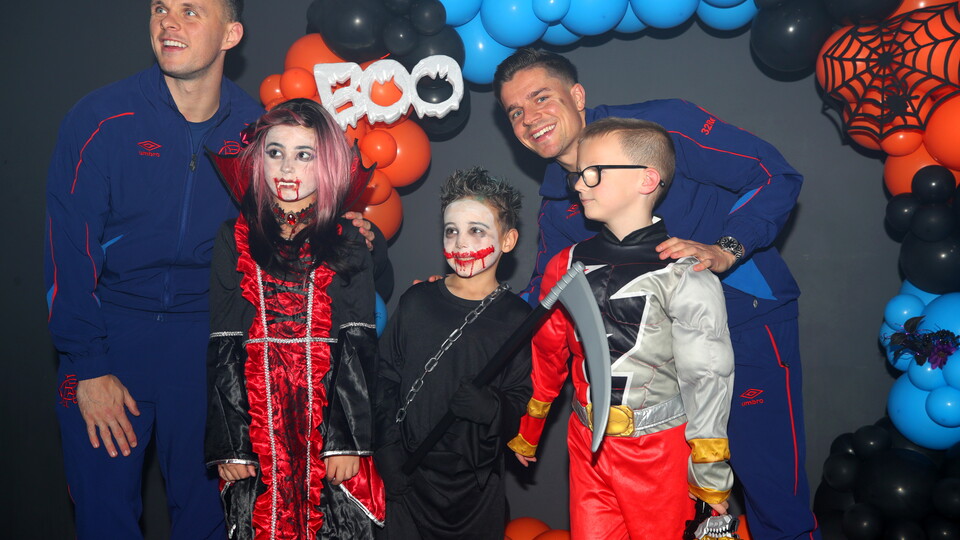 Five people dressed in Halloween costumes standing in front of a backdrop of balloons.