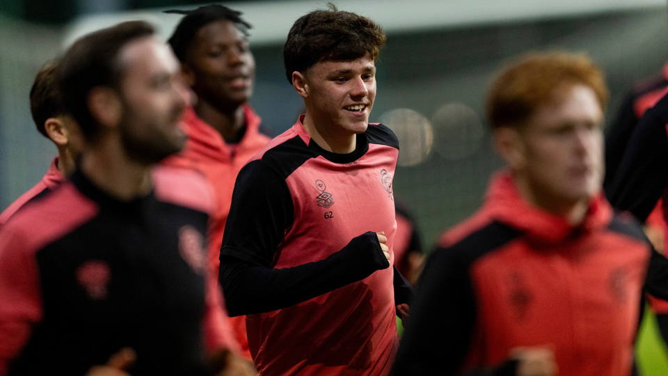 Six football players wearing red and black training shirts walk across a pitch.