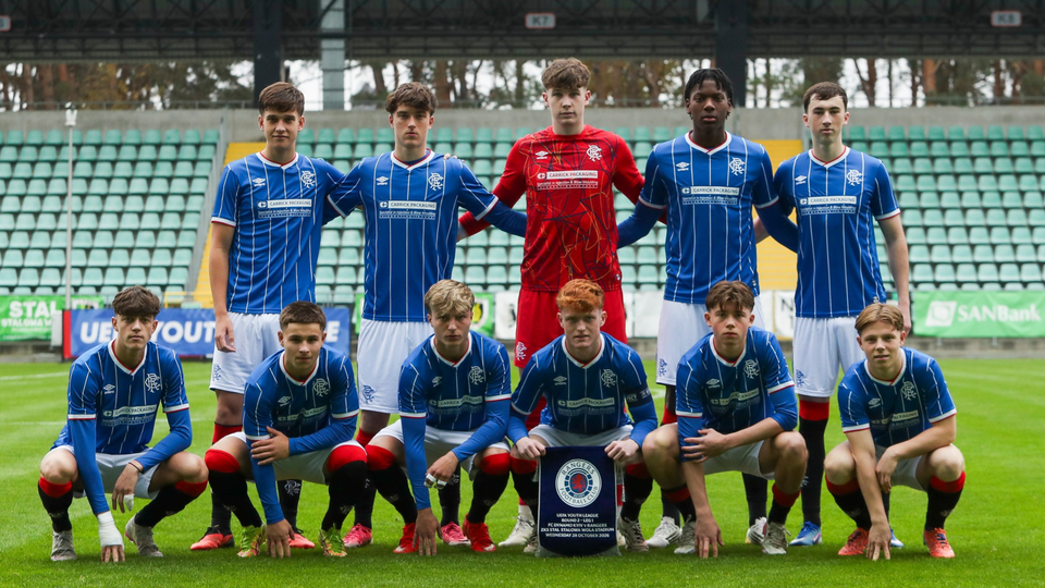 Eleven young players in blue and white kits pose for a team photograph with a trophy.