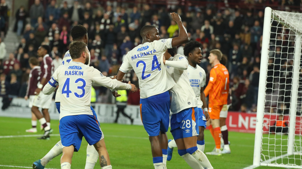 Players celebrate a goal in a football match, wearing white and blue kits with numbers 24, 43, and 18.