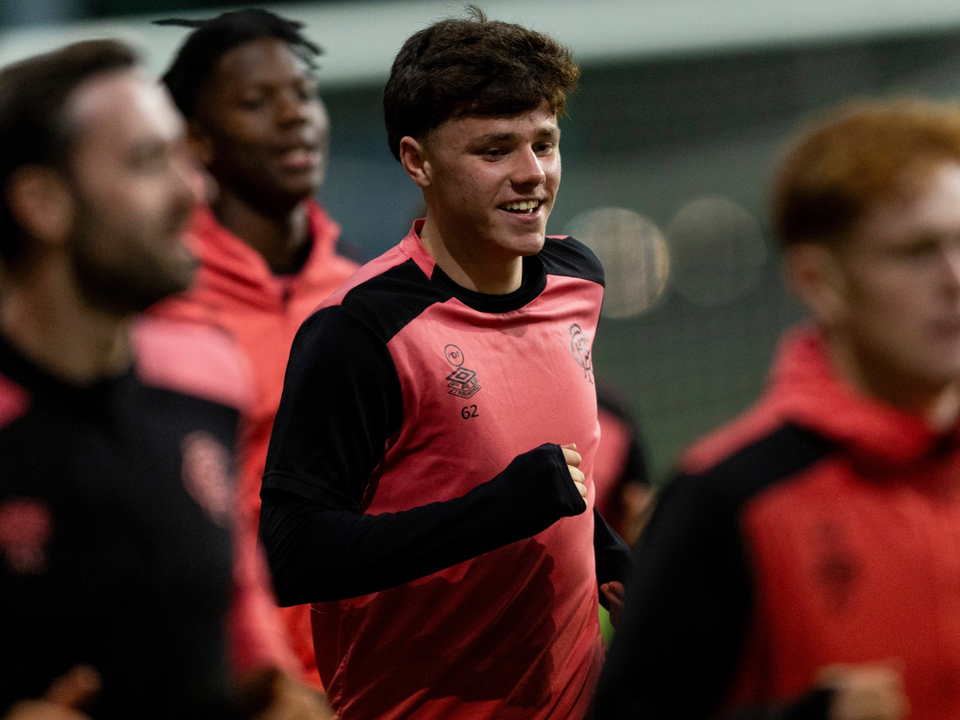 Six football players wearing red and black training shirts walk across a pitch.